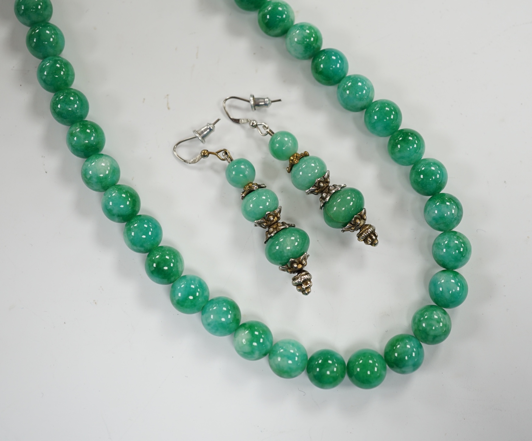 A single strand jadeite bead necklace, 41cm and a pair of jadeite earrings, stamped 18k.